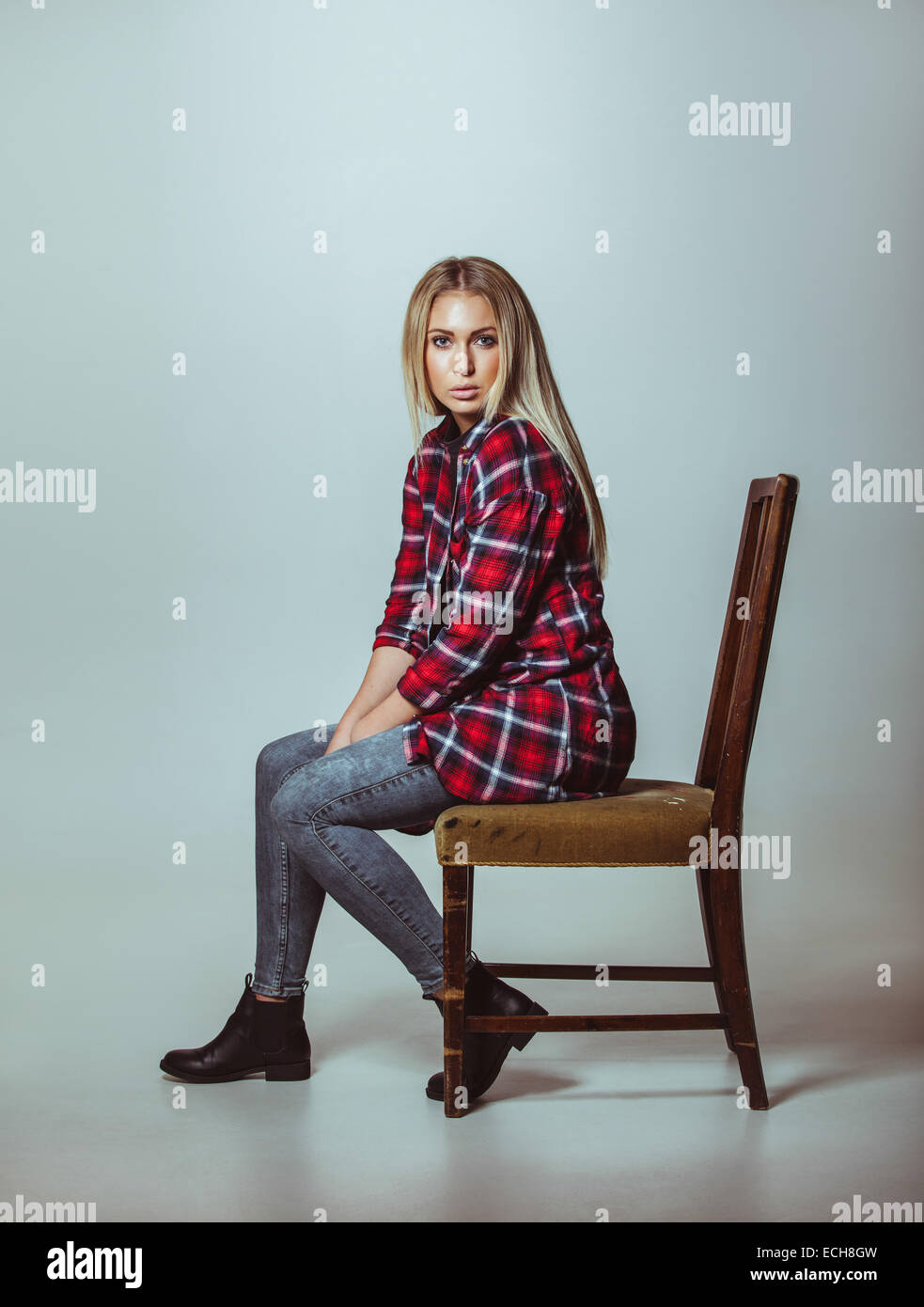 Porträt der schönen jungen Frau in casual-Outfit auf Stuhl sitzend. Kaukasische weibliches Modell Blick in die Kamera. Stockfoto