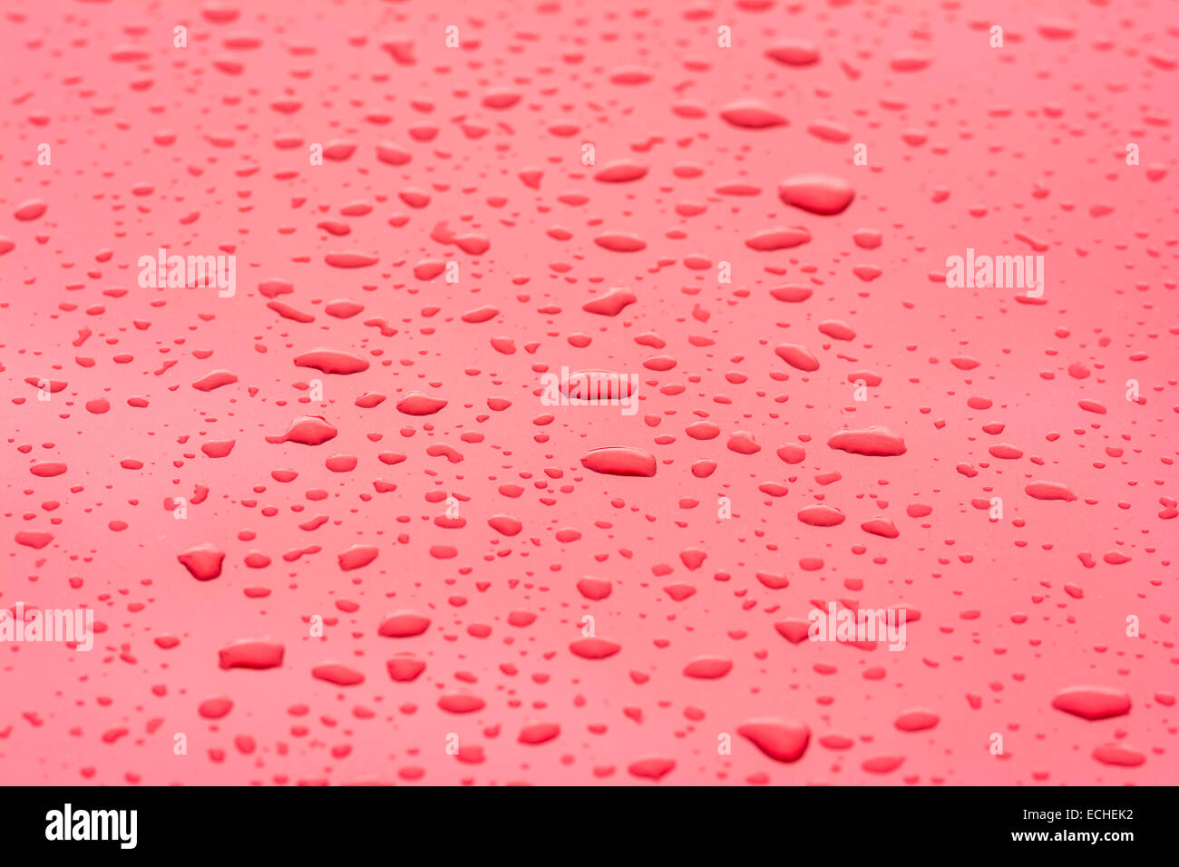 Regentropfen hautnah auf rote metallische Oberfläche Stockfoto