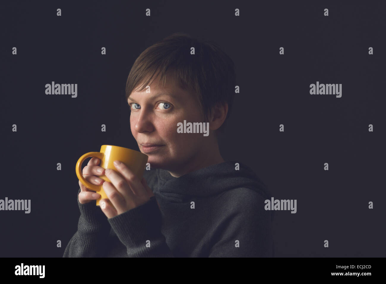 Schöne kaukasischen erwachsenen Frau trinken Kaffee oder Tee im dunklen Raum. Selektiven Fokus mit geringen Schärfentiefe. Stockfoto