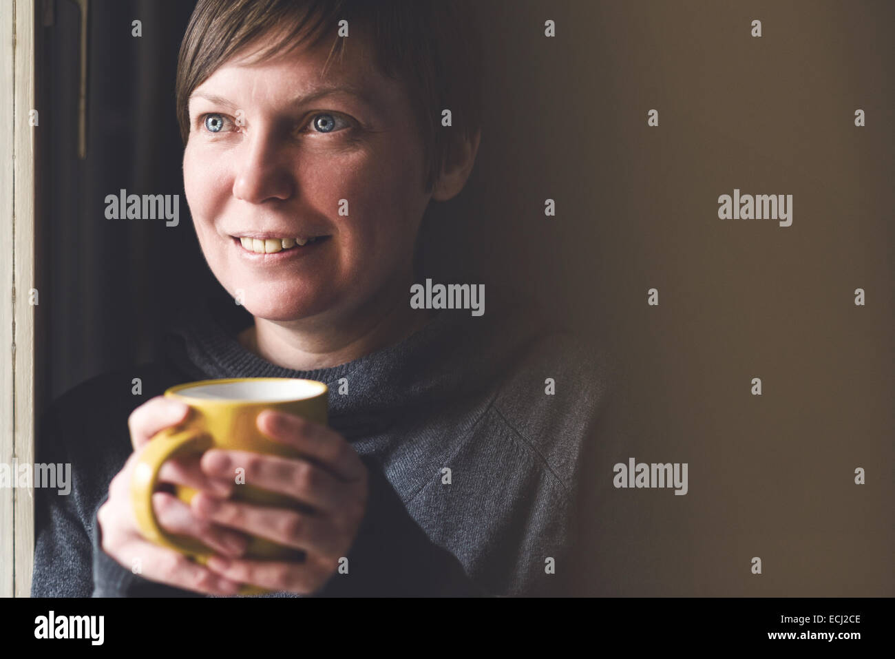 Schöne kaukasischen Erwachsenen lächelnde Frau trinken und genießen Kaffee im dunklen Raum. Stockfoto
