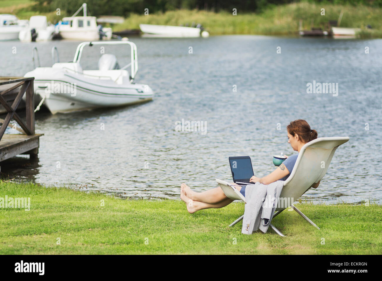 Voller Länge Seitenansicht des Reife Frau mit Laptop auf Liegestuhl am Seeufer Stockfoto