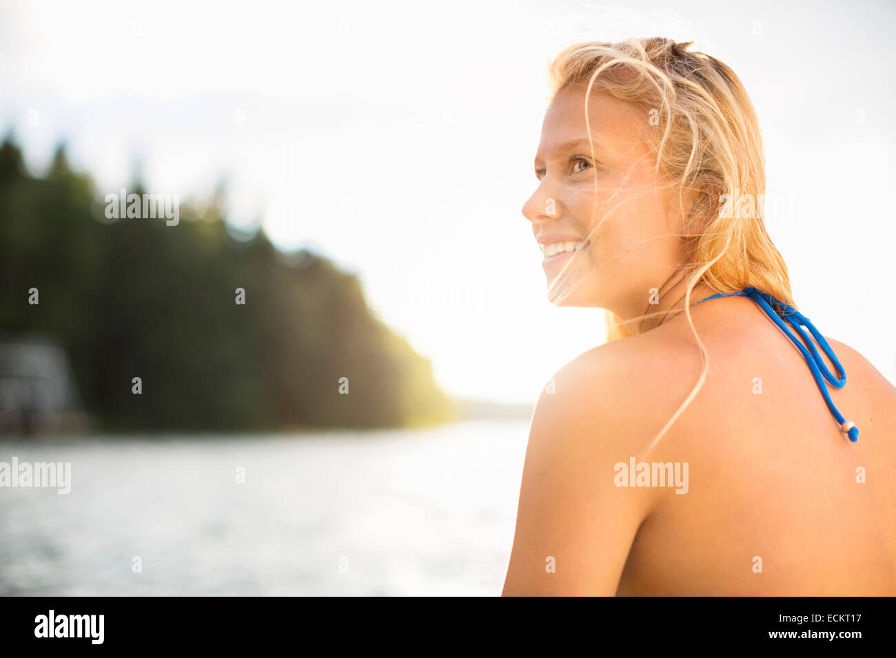 Rückansicht des lächelnden Frau Wegschauen am Seeufer gegen klaren Himmel Stockfoto