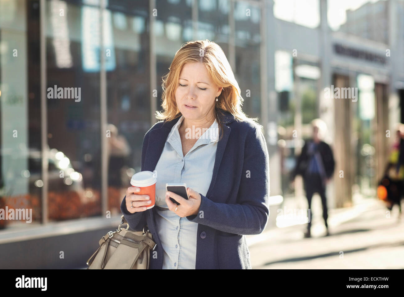 Geschäftsfrau mit Handy und Einweg-Kaffeetasse halten während des Gehens auf Bürgersteig Stockfoto