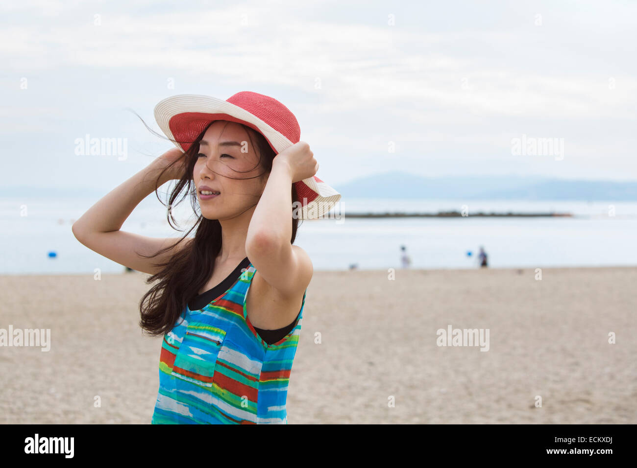 Eine Frau an einem Strand in Kobe, halten ihren Hut auf. Stockfoto