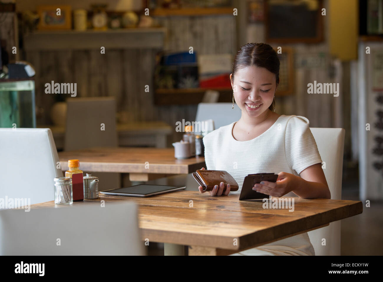 Frau sitzt an einem Tisch in einem Café, hält die Rechnung und ihre Geldbörse, lächelnd. Stockfoto