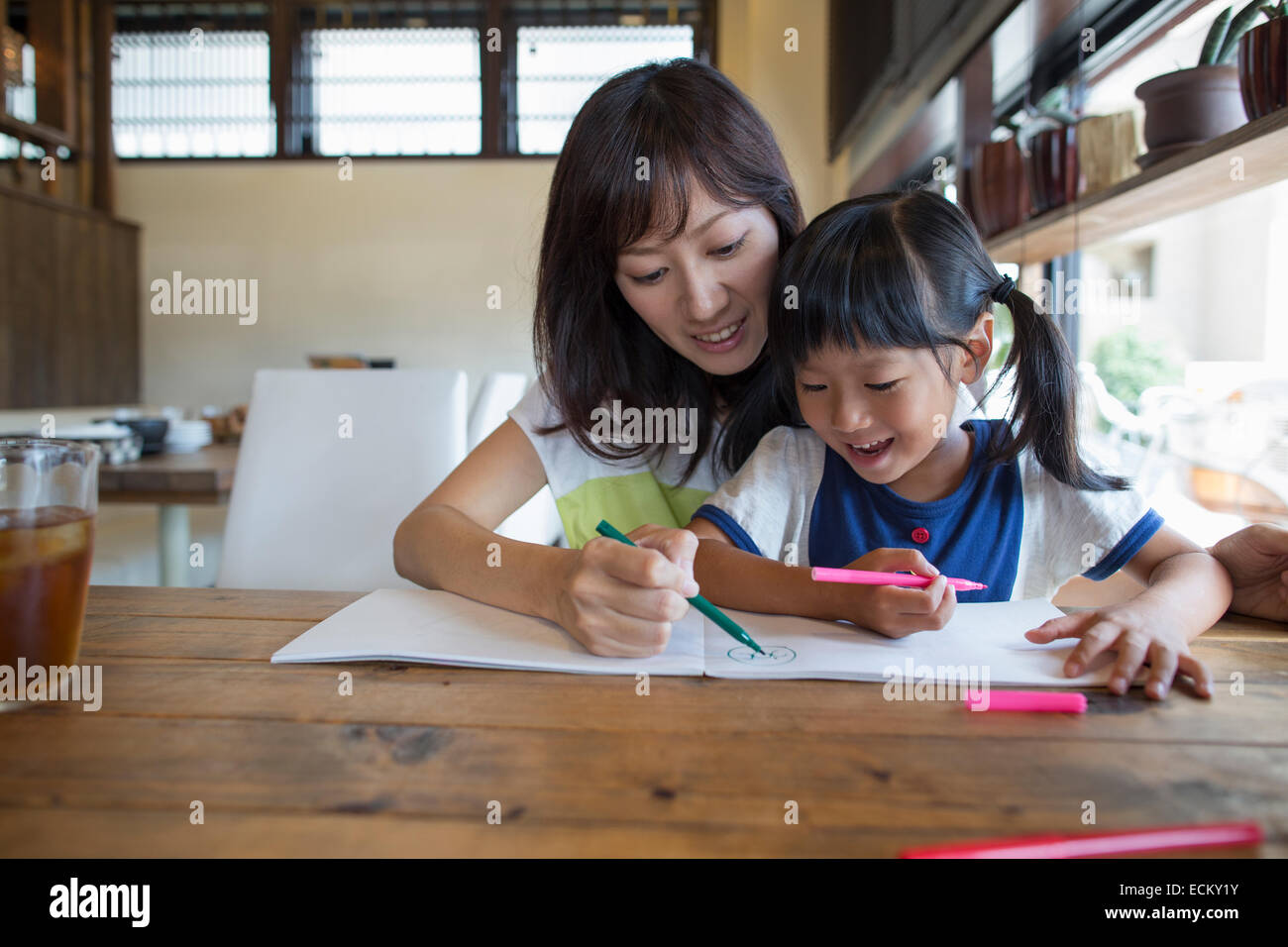 Mutter und Tochter sitzen an einem Tisch, zeichnen mit Filzstift Stifte, lächelnd. Stockfoto