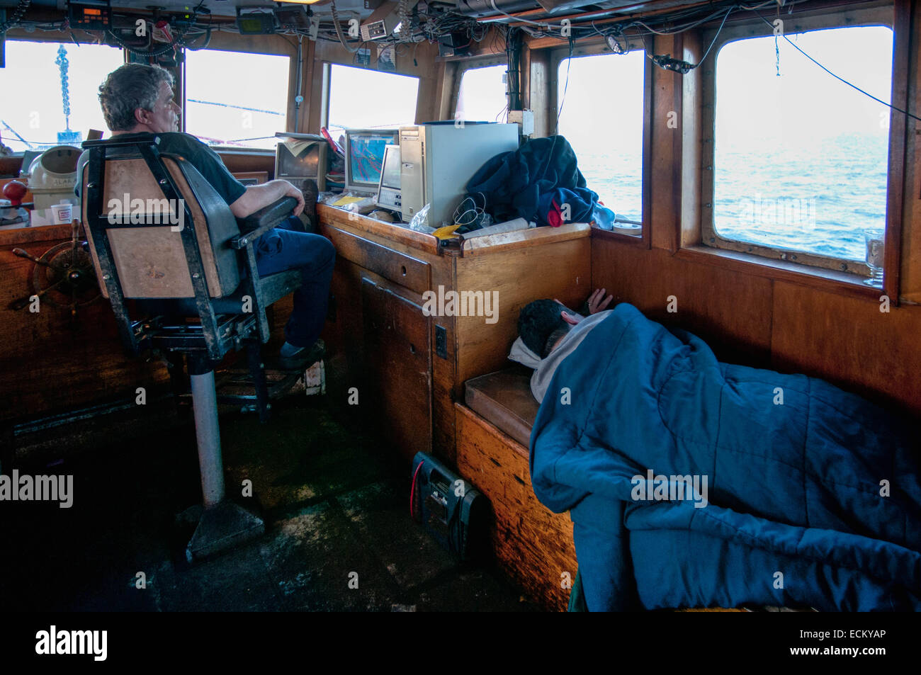 Kapitän wacht auf elektronische Daten in Kabine der Fischerei Dragger während Crewman NAP. Stockfoto