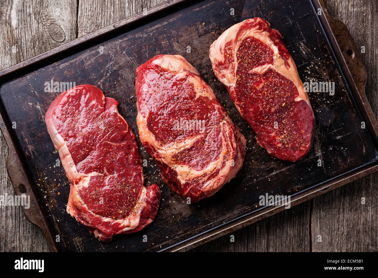 Drei schneidet rohes Frischfleisch Steaks und Gewürze auf dunklem Hintergrund Stockfoto