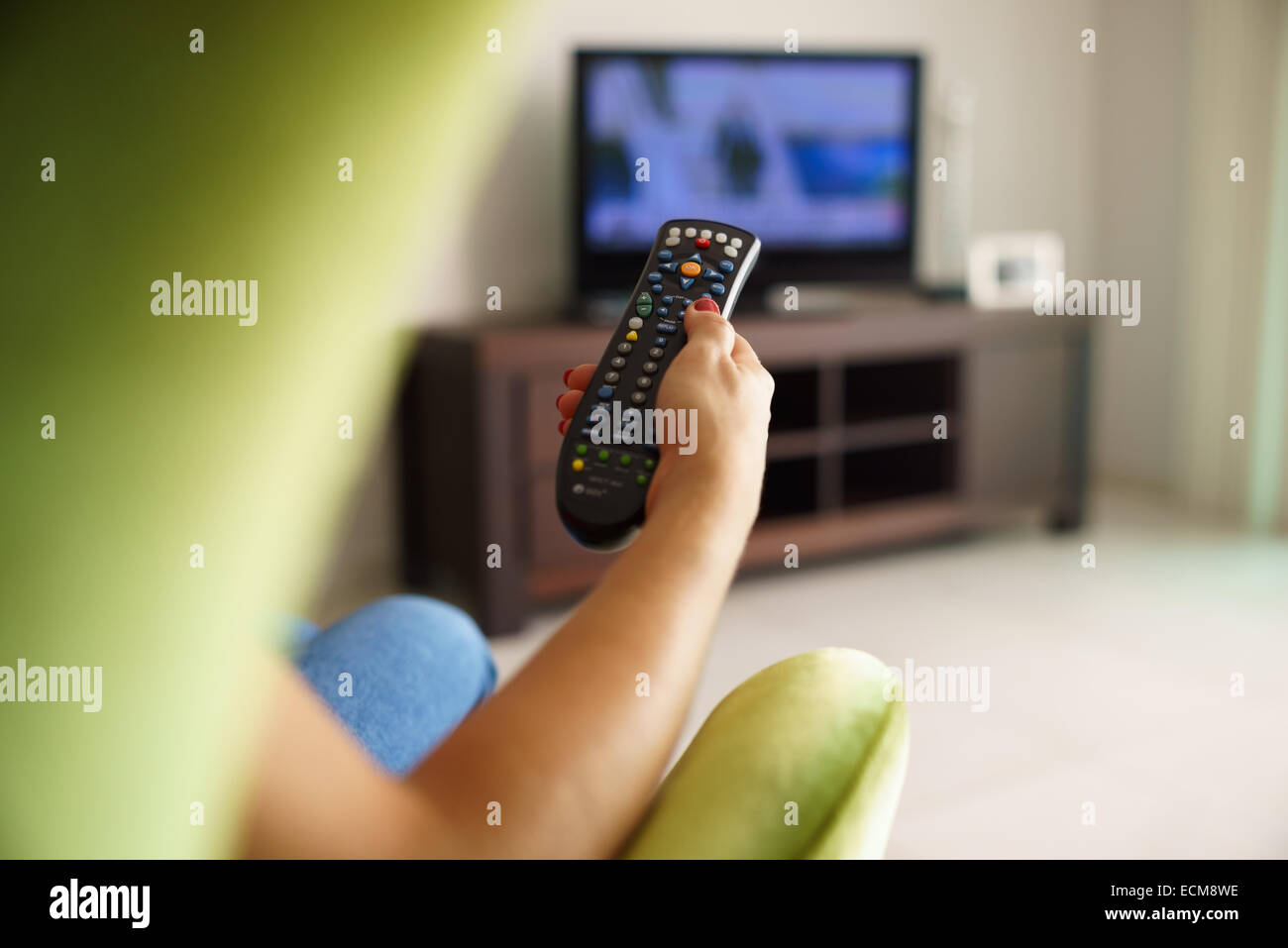 Über die Schulter-Blick des Mädchens auf Sofa sitzen halten tv remote und Surfen Programme im Fernsehen Stockfoto
