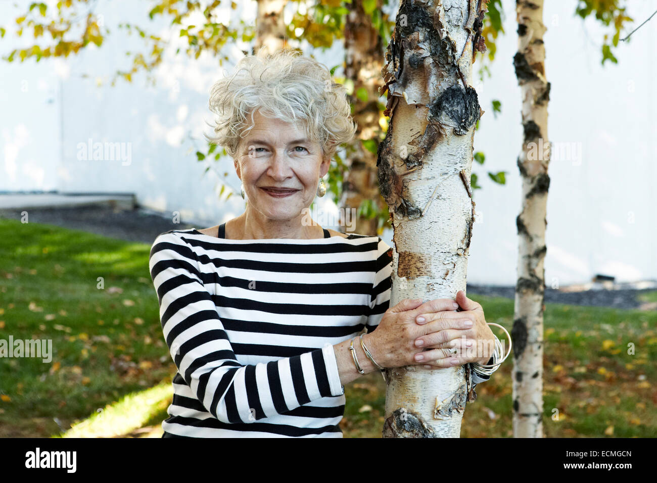 Schöne aktive 65 jährige Senior stützte sich auf Birke Stockfoto