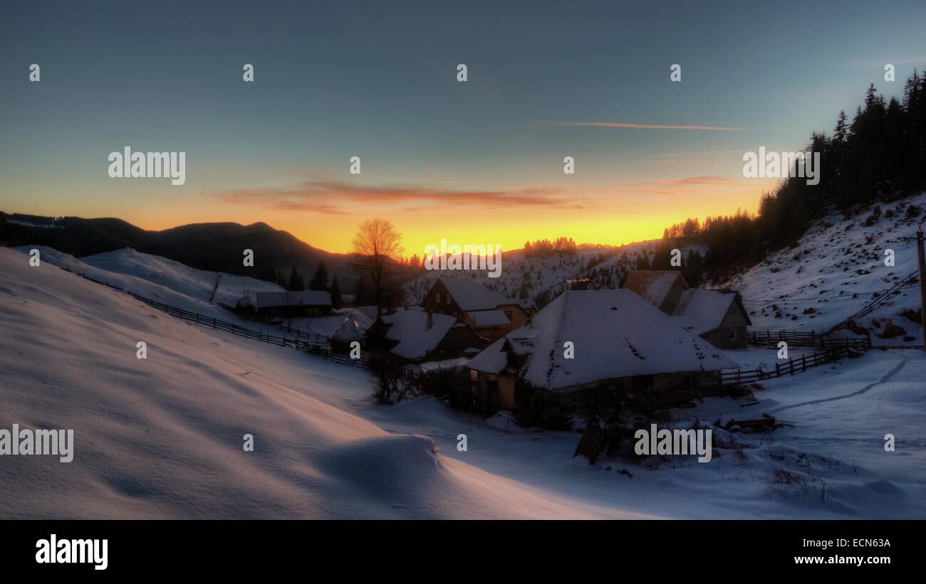 Winter-Sonnenuntergang über Dorf Fundata. Berglandschaft mit Häusern, die unter dem Schnee in Karpaten, Rumänien Stockfoto