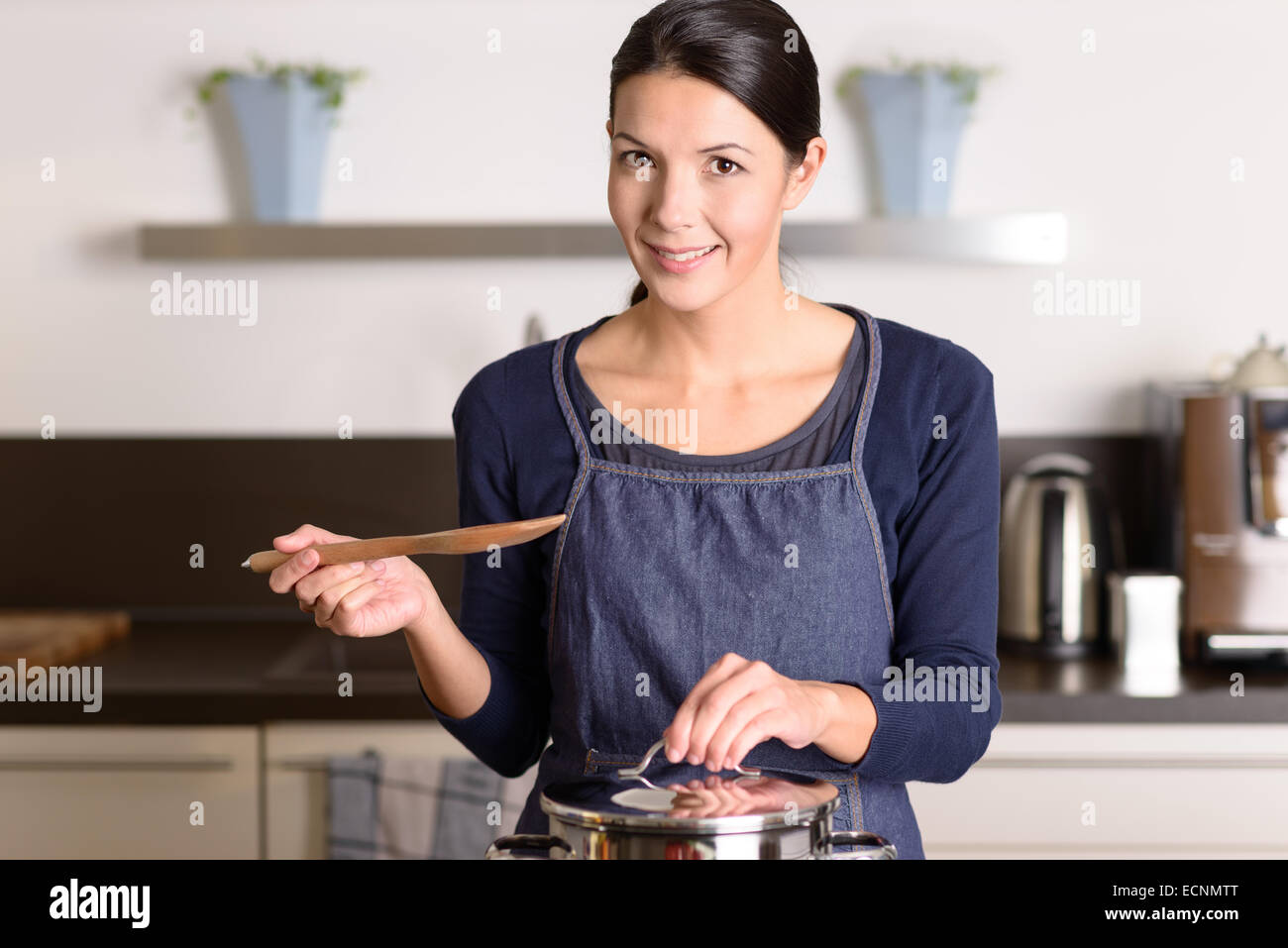 Junge Frau, die das Essen zum Abendessen über dem Herd in ihrer Küche stehen, halten den Deckel von einem Edelstahl-Topf kochen und Stockfoto