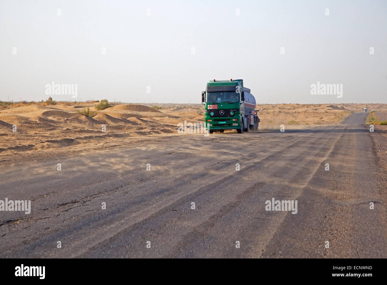 LKW-Durchquerung der Wüste Karakum in Turkmenistan und wind bläst Sand von den Dünen auf der anderen Straßenseite Stockfoto