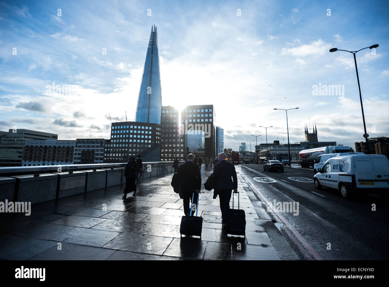 London, UK - 17. Dezember 2014: Geschäftsleute mit Rollwagen überqueren die Sonne scheint hinter Gebäuden und The Shard London Bridge Stockfoto