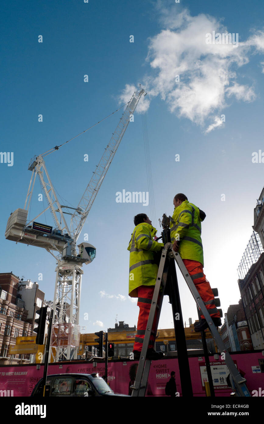 Zwei Arbeiter Arbeiter stehen auf Leitern arbeiten an Leuchten und Kran auf der Baustelle in der Oxford Street in London UK KATHY DEWITT Stockfoto