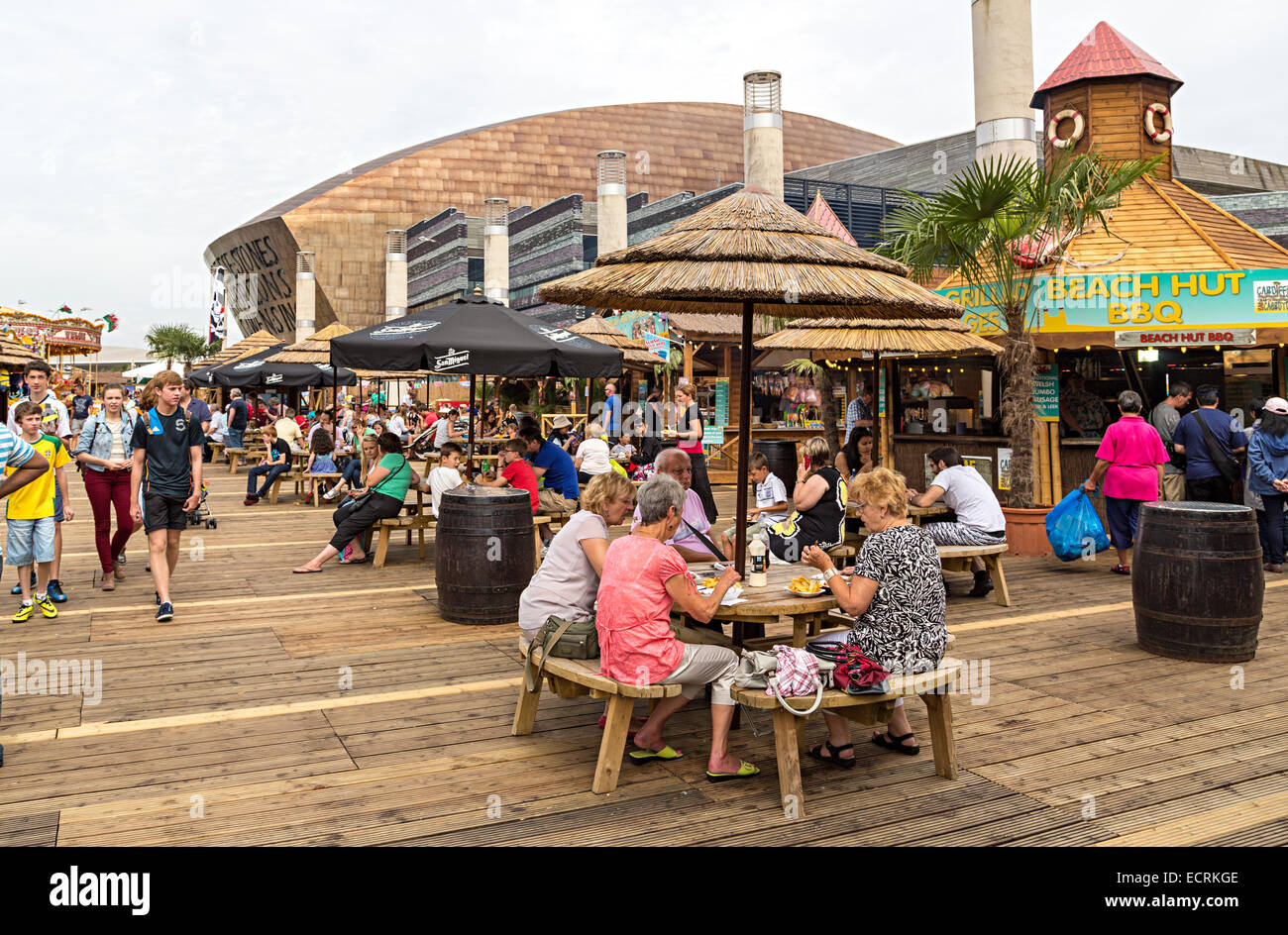 Leute sitzen an Tischen Open-Air am Jahrmarkt in Cardiff Bay mit dem Millennium Centre im Hintergrund, Wales, UK Stockfoto