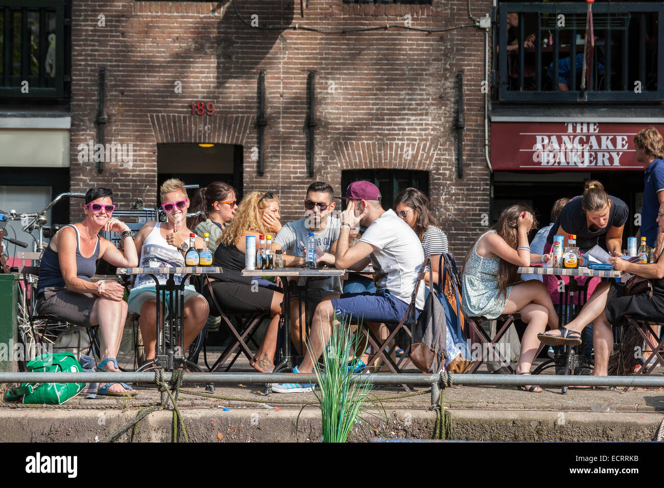 Amsterdam-Pfannkuchen-Bäckerei-Restaurant am Prinsengracht Kanal. Leute sitzen auf dem Rand des Wassers. Aus dem Kanal zu sehen. Stockfoto