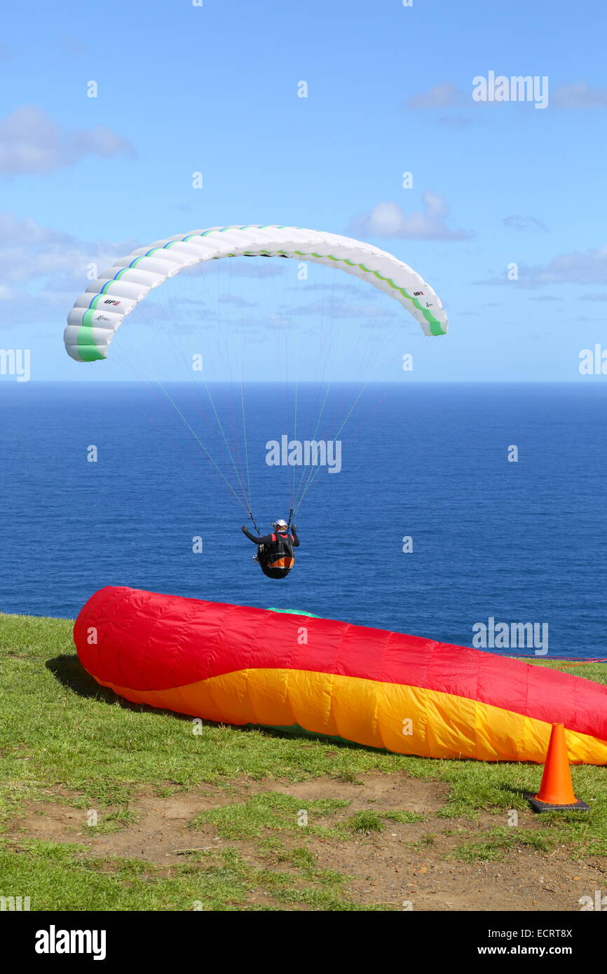 Ein Mann fliegt seinen Gleitschirm und schwebt über dem Pazifischen Ozean vor kahlen Hügel, New-South.Wales, Australien als eine andere ist bereit. Stockfoto