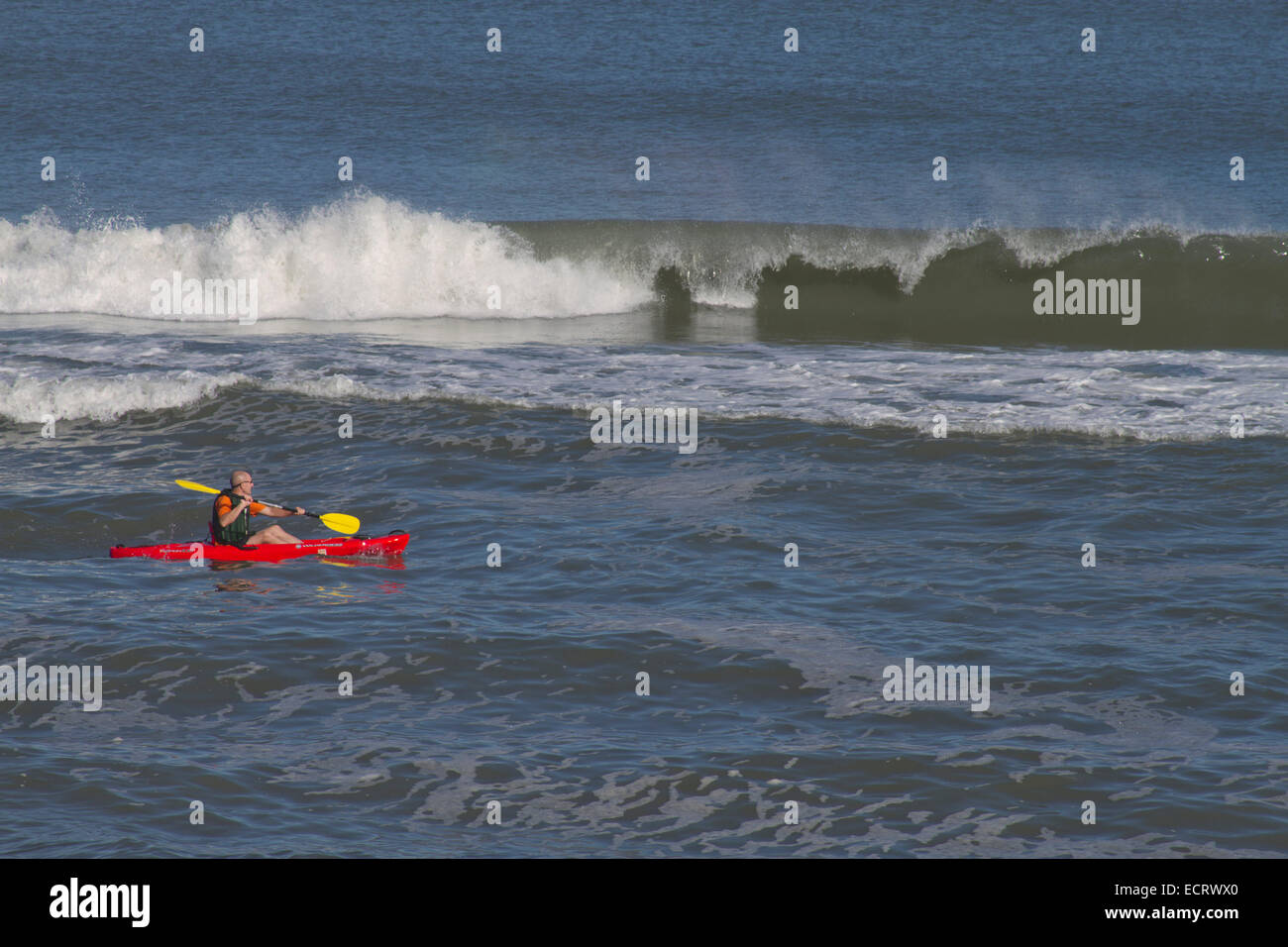 Ein Mann in einem hellen Rot und Gelb Kajak ruder Paddel von einem großen, brechen Ocean Wave Stockfoto