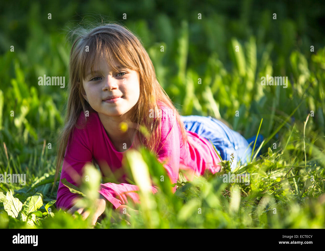 Niedliche kleine Mädchen im grünen Rasen im Park. Stockfoto