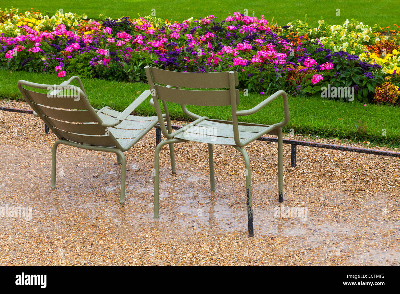 Nassen Metall Sessel im verregneten Park mit bunten Blumen in Paris Stockfoto