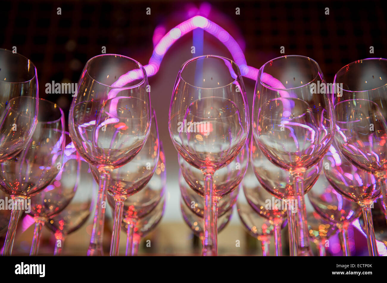 Weingläser, aufgereiht auf einer Bar vor einem Neon-Licht. Stockfoto