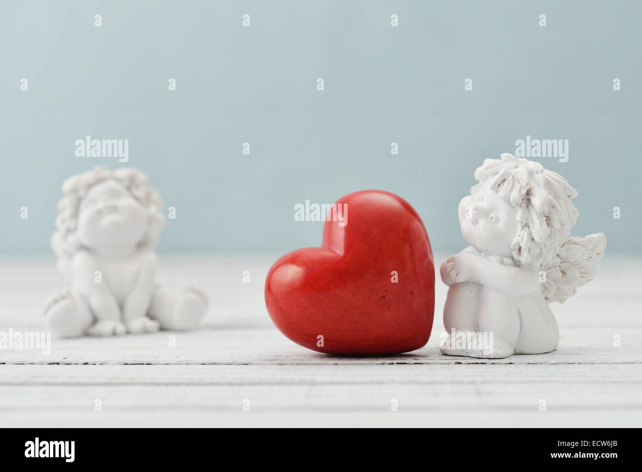 Statuetten von kleinen Engeln mit steinernen Herzen auf hellem Hintergrund Stockfoto