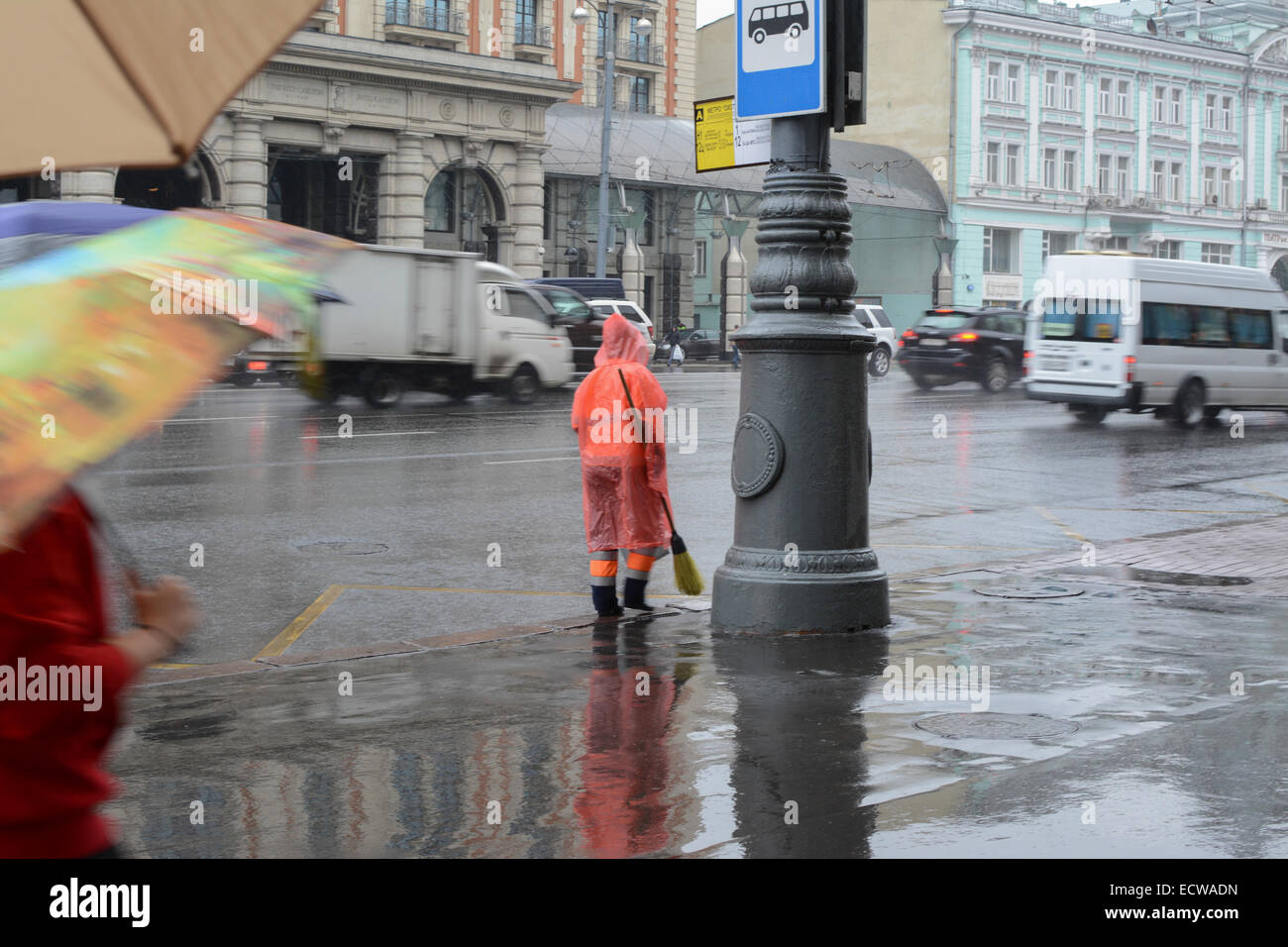 A Straße Reiniger trägt eine helle orange Regenjacke in einer verregneten Straße in Moskau Stockfoto