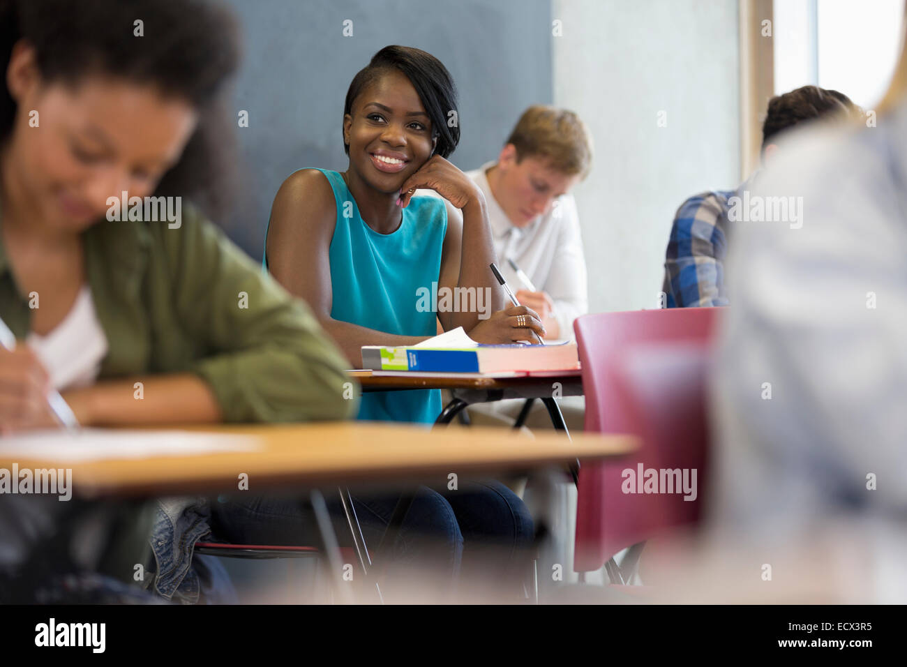 Lächelnde Studenten sitzen am Schreibtisch mit Hand am Kinn Stockfoto