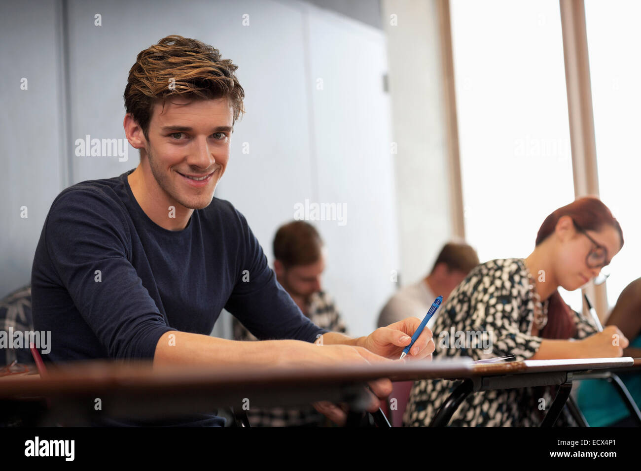 Männlichen Studenten in die Kamera Lächeln und sitzen am Schreibtisch während der Vorlesung Stockfoto