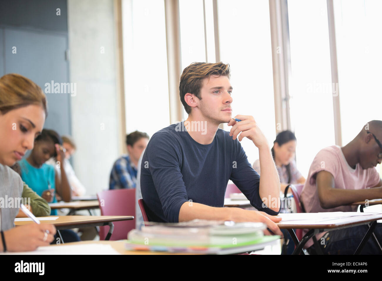Männliche Schüler mit Hand am Kinn während der Vorlesung mit anderen Studenten im Hintergrund Stockfoto