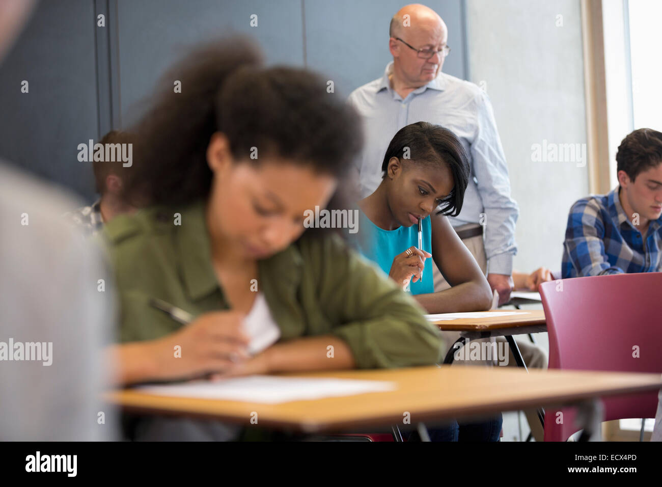 Lehrer zu Fuß entlang Schreibtische und Studenten während Tests überprüfen Stockfoto