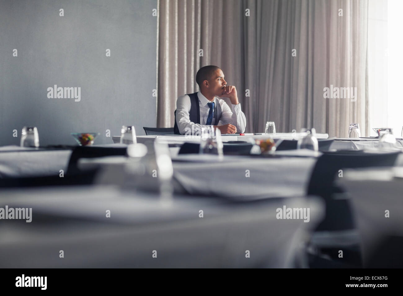 Porträt des jungen Mann sitzt am Tisch im leeren Konferenzraum Blick durch Fenster Stockfoto