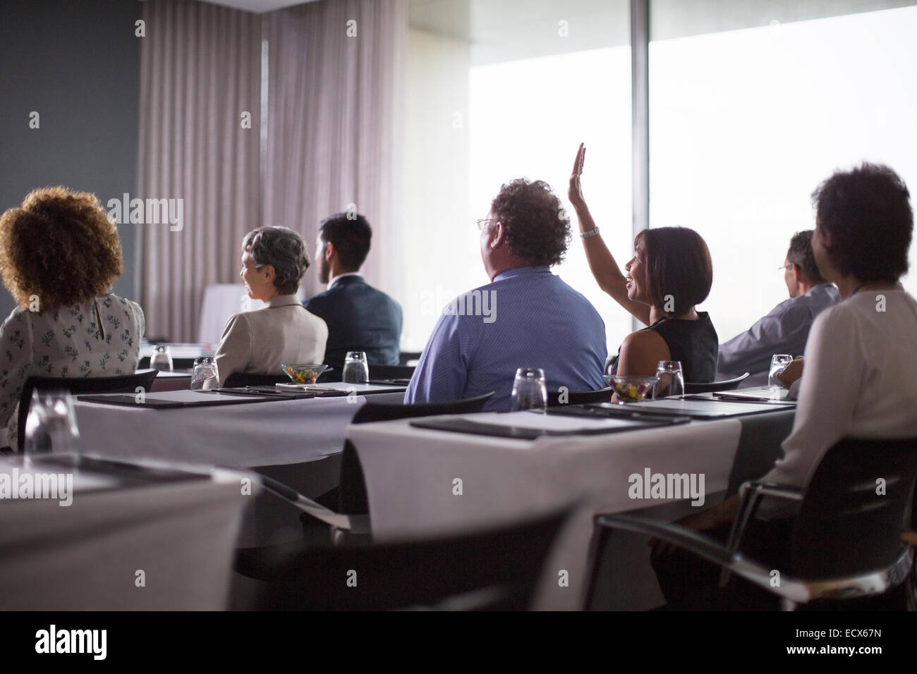 Mittlere Gruppe von Konferenzteilnehmern sitzen im Konferenzraum mit Frau Hand heben Stockfoto