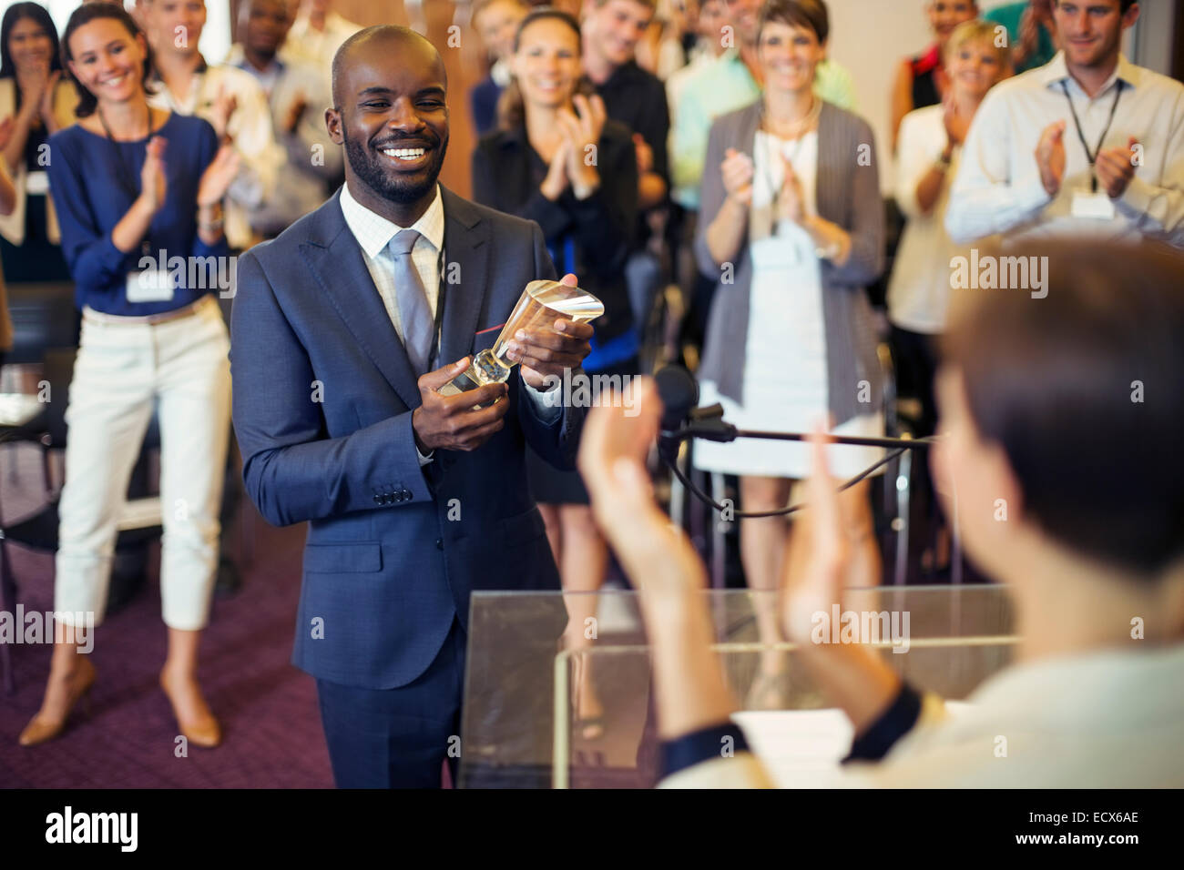 Porträt des jungen Mann, der Trophäe, stehend im Konferenzraum, hält lächelnd zu applaudierenden Publikum Stockfoto