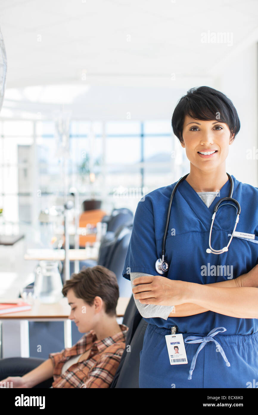 Porträt des Arztes mit verschränkten Armen und Patienten in der medizinischen Behandlung im Hintergrund Stockfoto