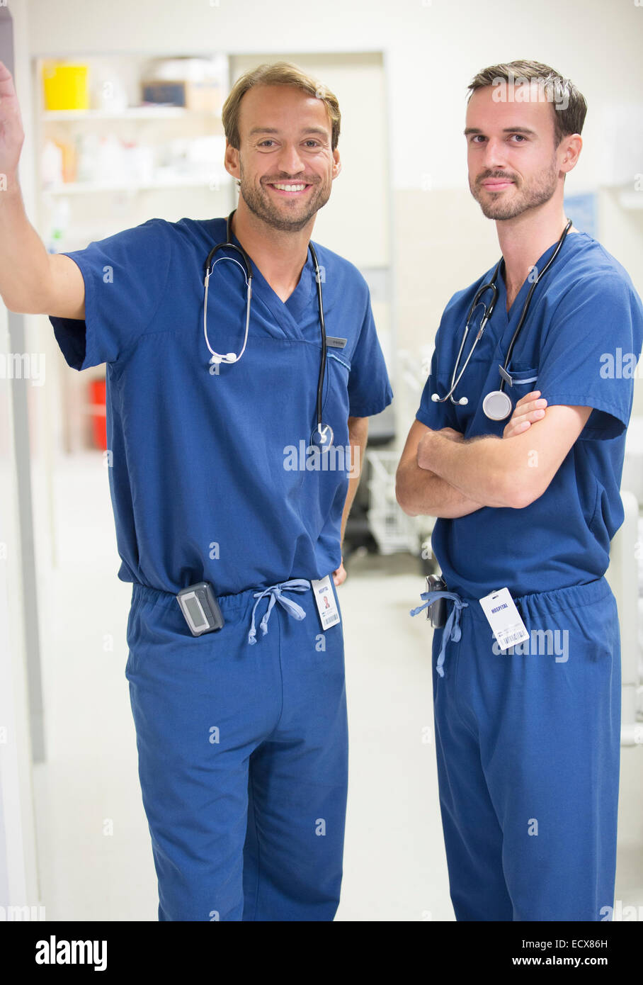 Zwei männliche Ärzte tragen lächelnd Scrubs – Die Anfänger stehen im Krankenhaus Stockfoto