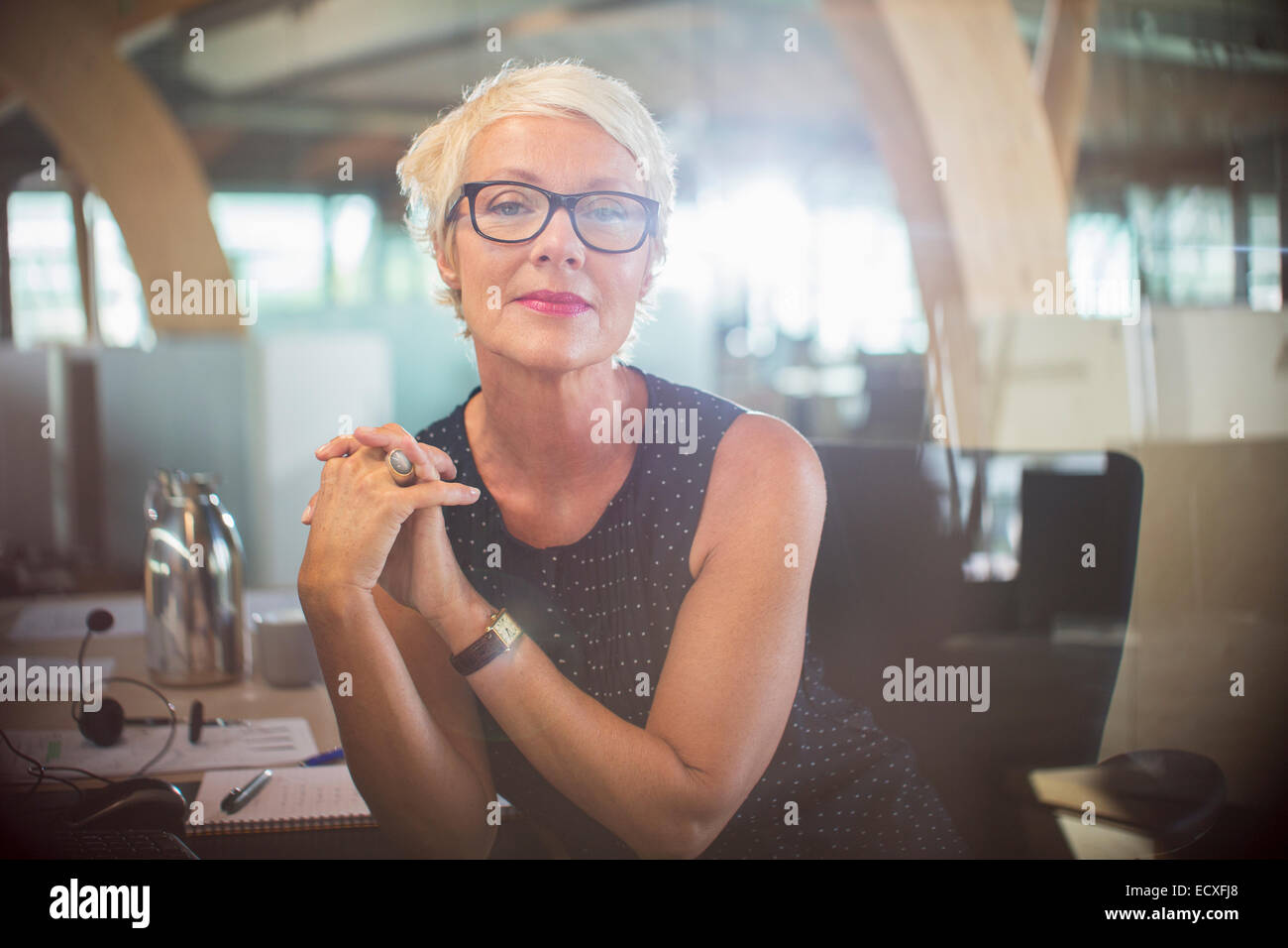 Geschäftsfrau, die mit den Händen umklammert am Schreibtisch sitzen Stockfoto