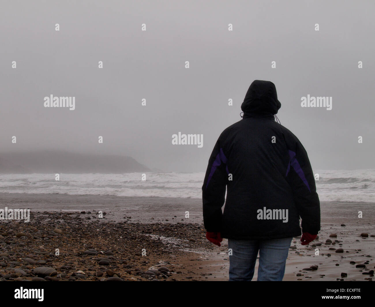 Frau am Strand an einem grauen nebliger Wintertag, Widemouth Bay, Bude, Cornwall, UK Stockfoto