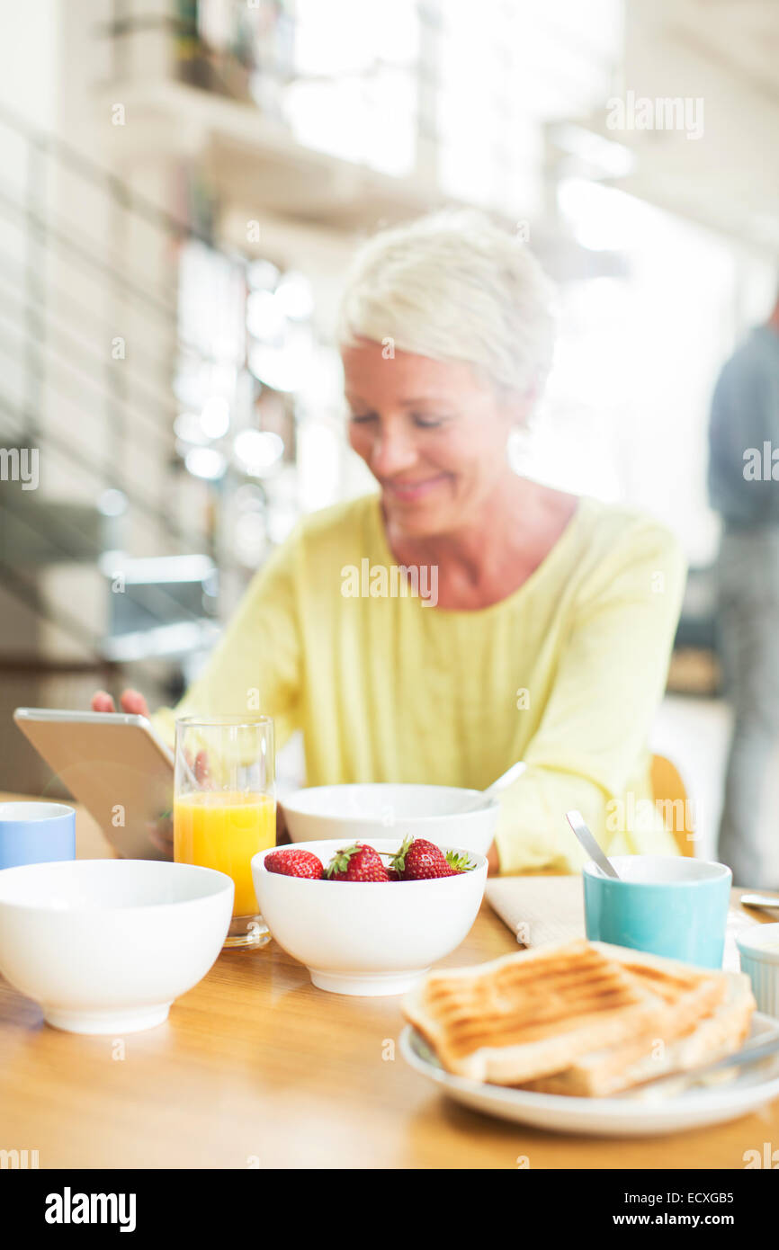 Ältere Frau mit digital-Tablette am Frühstückstisch Stockfoto