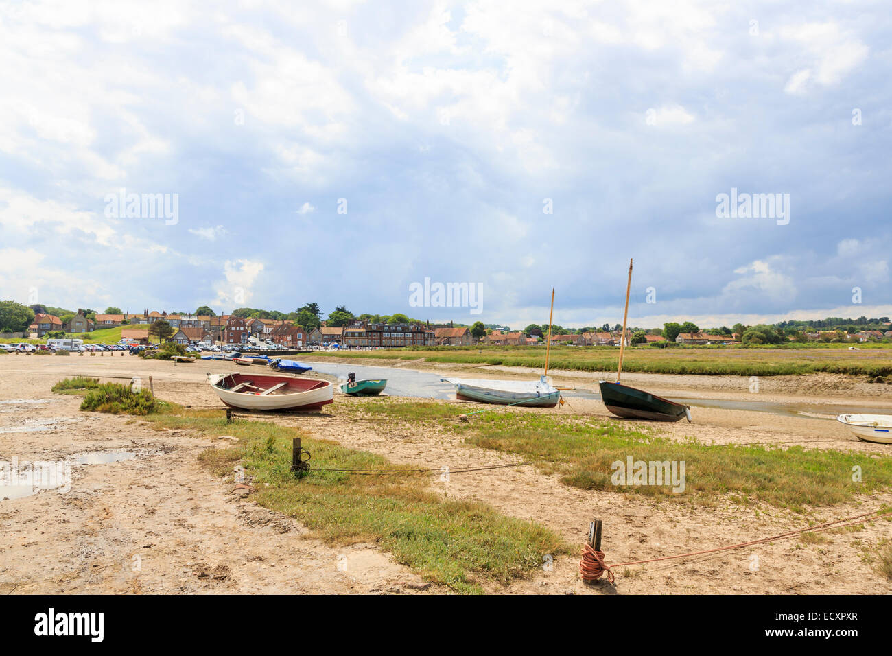 Boote vor Anker in Bach bei Ebbe im Hafen in Blakeney, einem Dorf in der Küstenstadt Norden Norfolk, Großbritannien im Sommer bei bewölktem Himmel: typische Landschaft Stockfoto