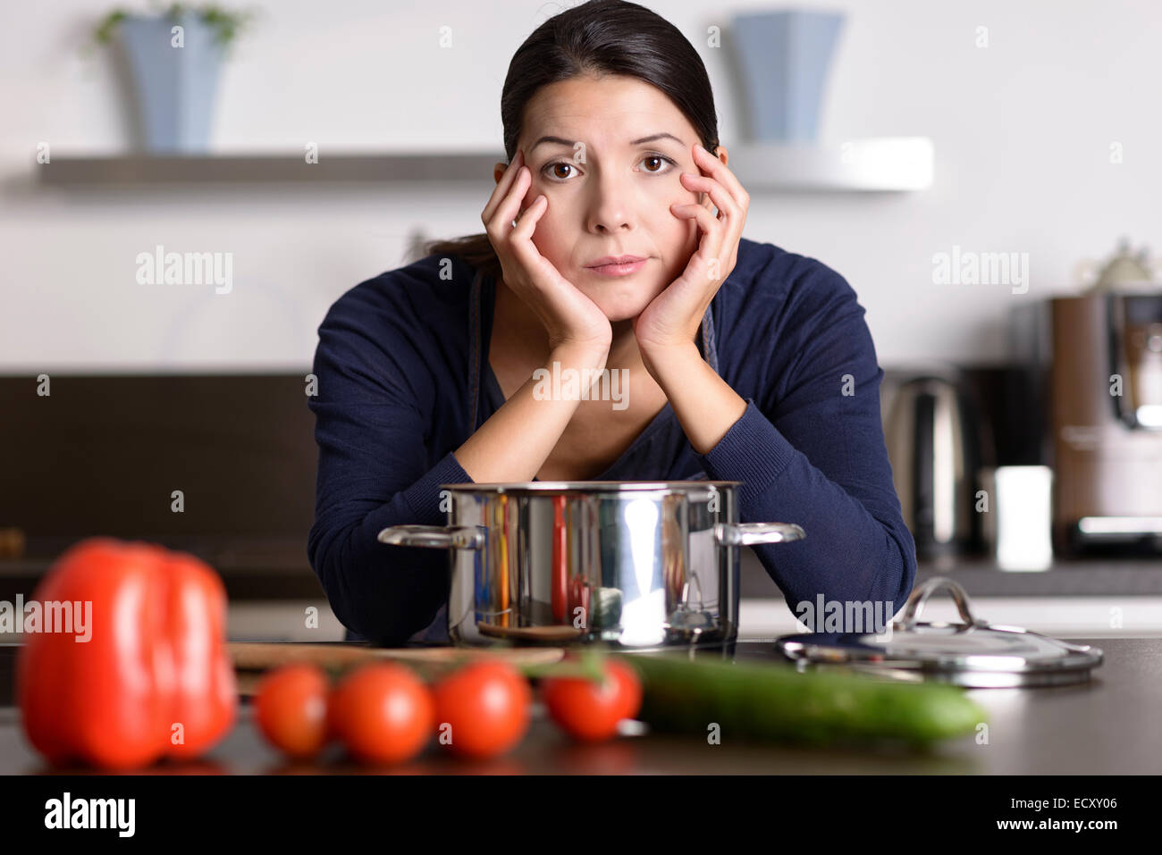 Unmotivierte attraktive junge Frau, die Vorbereitung des Abendessens stützte sich auf das Kochfeld beäugte die Kamera mit einem lustlosen glum Ausdruck als Stockfoto