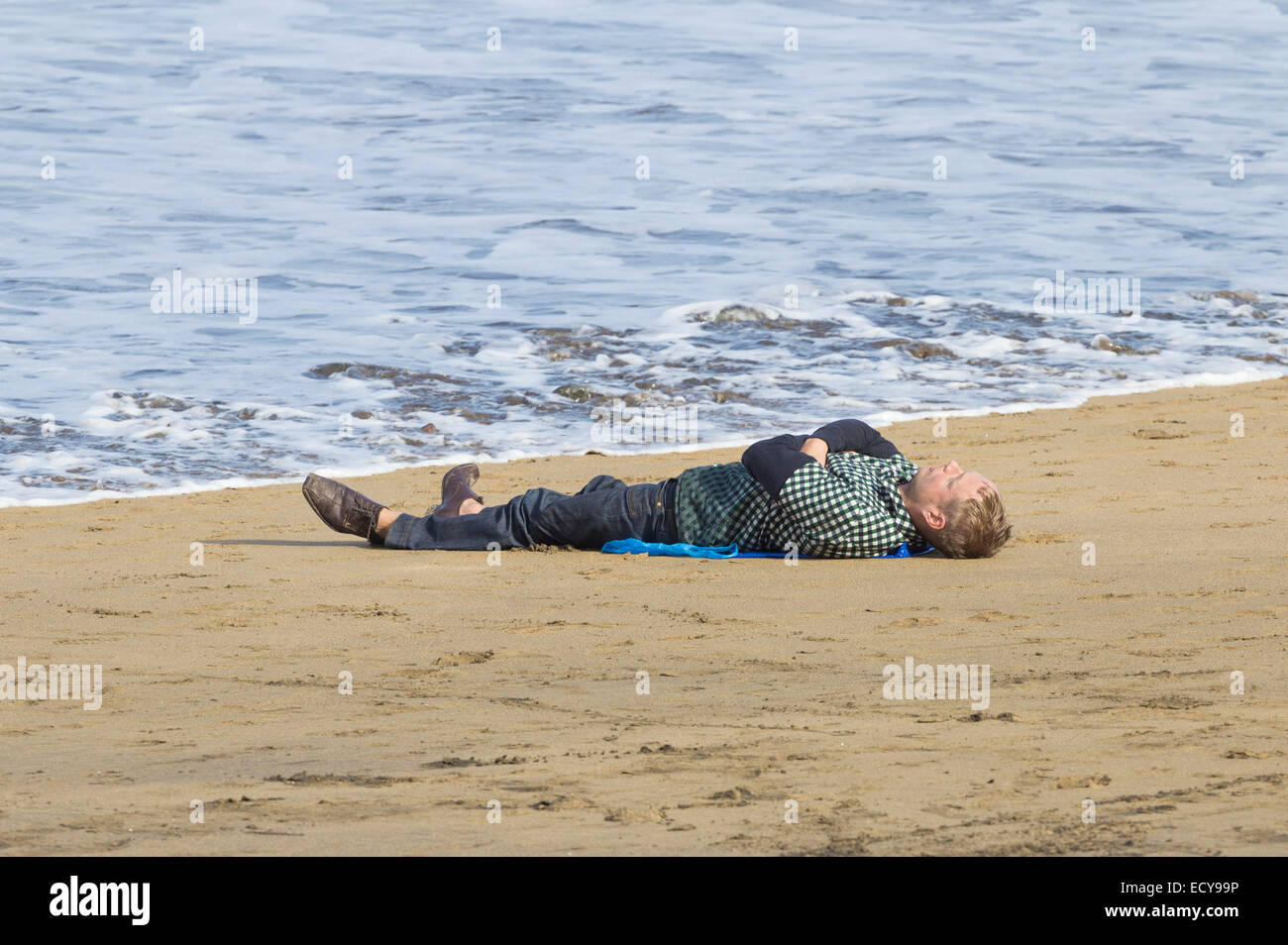 Mann dösen am Strand wird von der Flut getränkt. Stockfoto