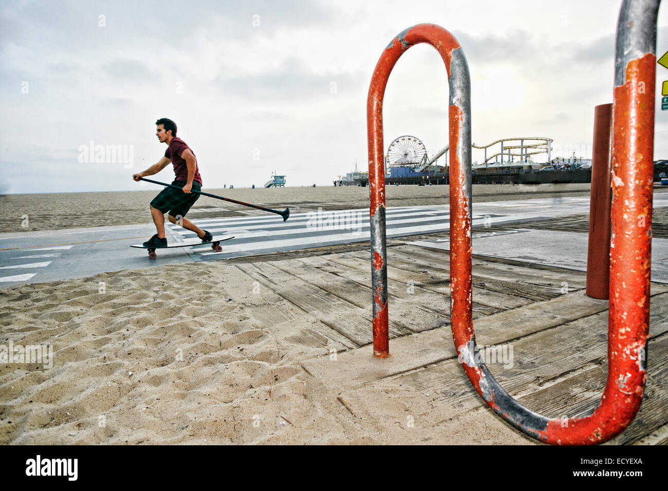 Kaukasischen Mann Skateboard mit Paddel Pol am Strand Stockfoto