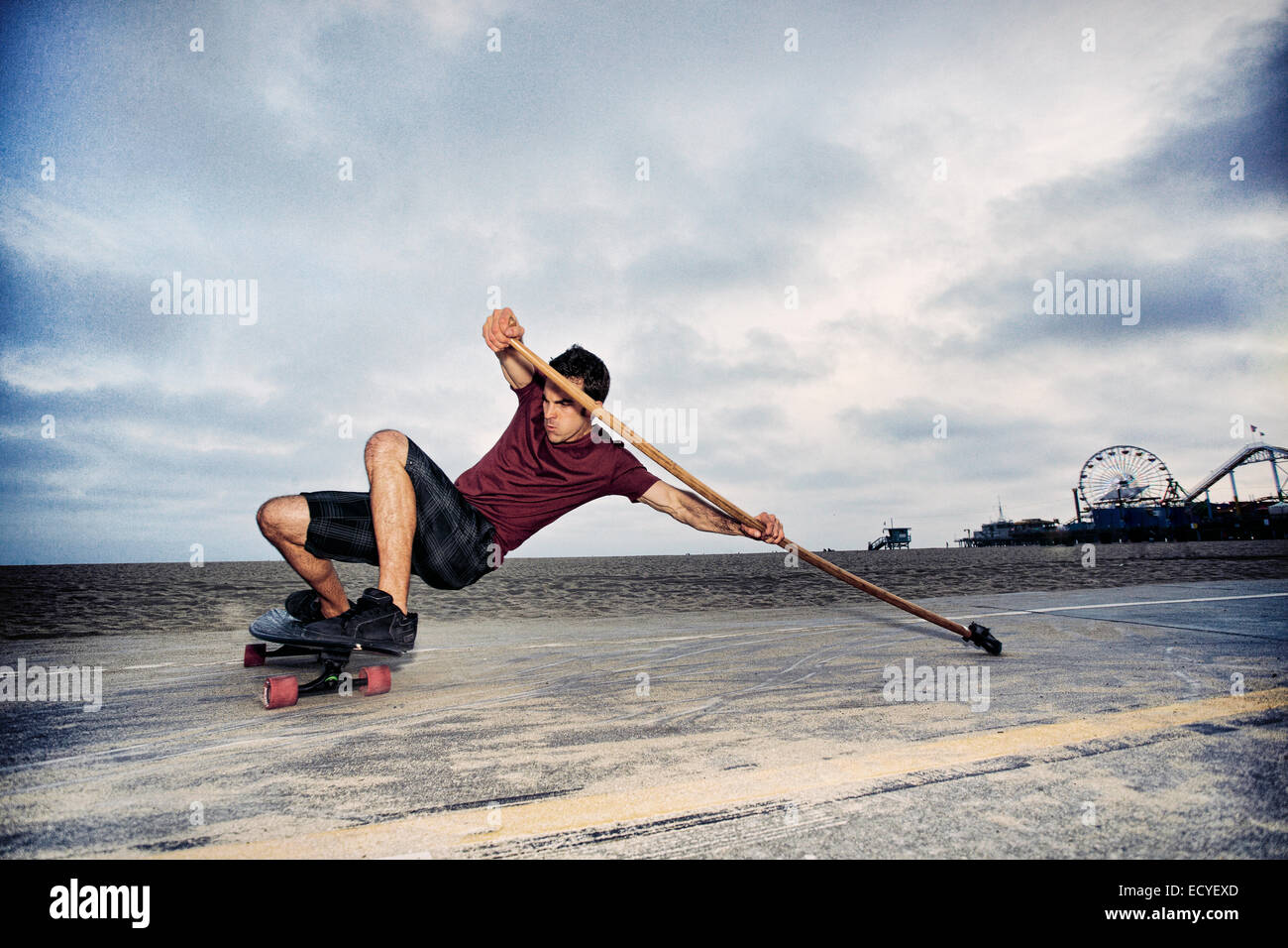 Kaukasischen Mann Skateboard mit Paddel Pol am Strand Stockfoto