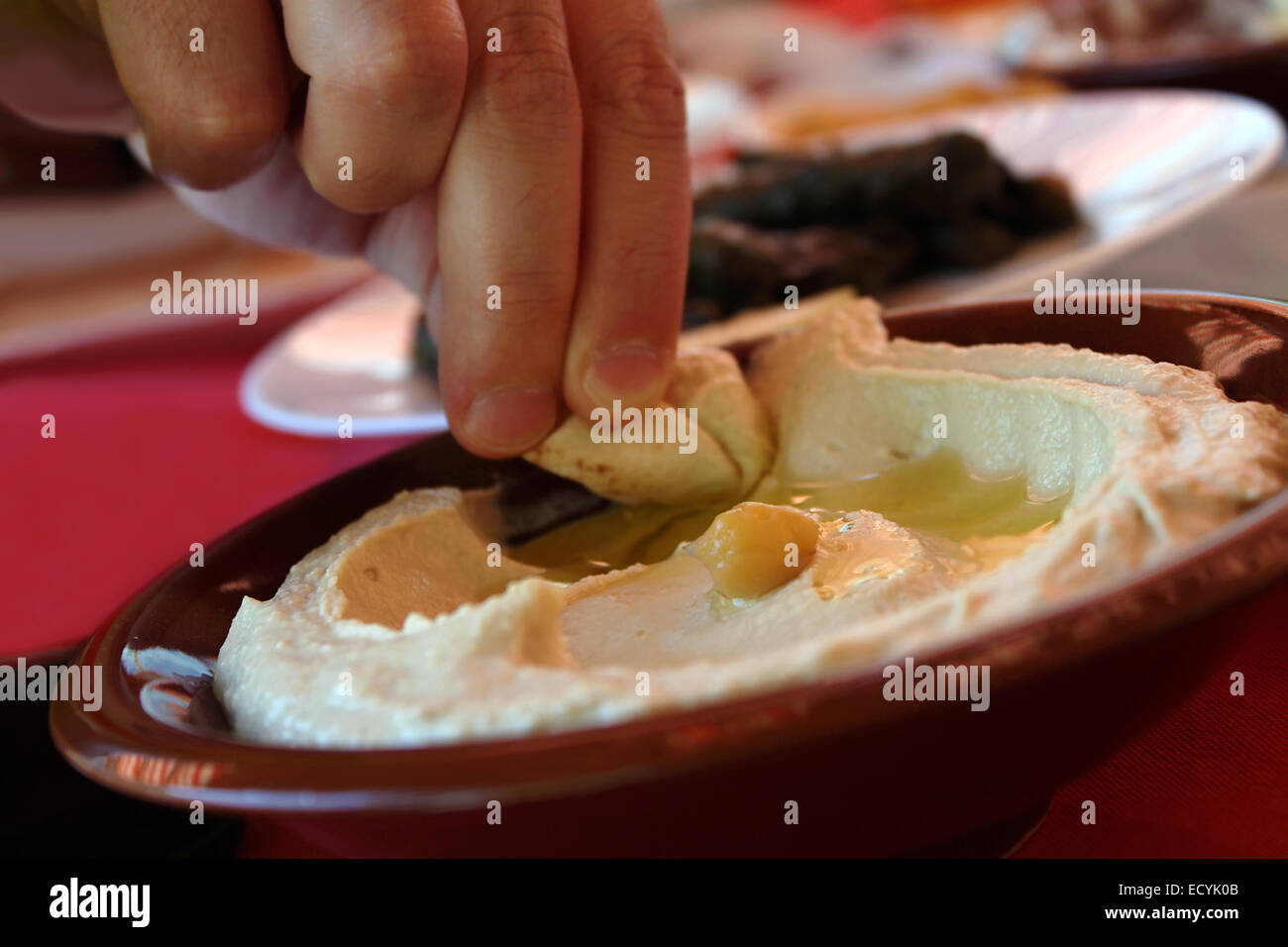 Ein Mann, ein Pita Brot Stück in einer traditionellen Hummus Platte eintauchen. Stockfoto