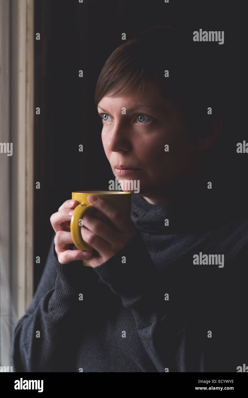 Einsame Frau trinken Kaffee am Fenster ihres Wohnzimmers Blick mit einem traurigen Blick auf ihrem Gesicht. Selektiven Fokus w Stockfoto