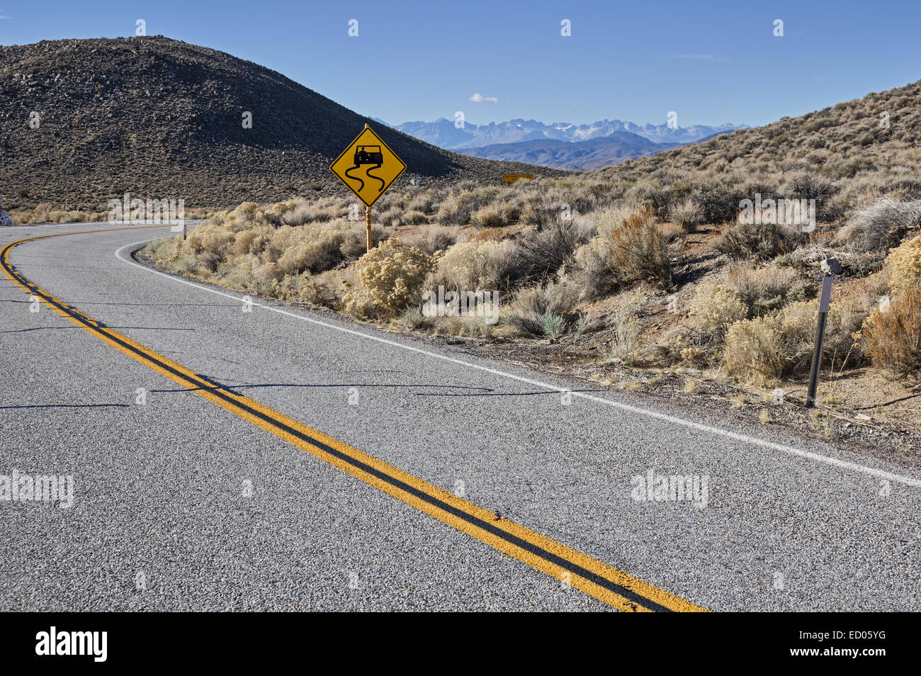 gekrümmte Straße mit rutschig Straßenschild und fernen Berge Stockfoto