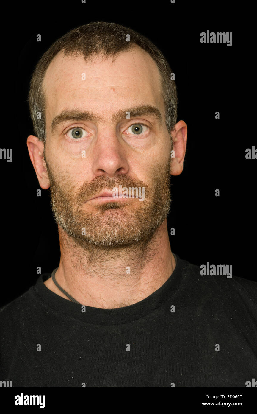 Porträt von einem robusten ergrauten Mann mittleren Alters mit schwarzen T-shirt auf schwarzem Hintergrund Stockfoto