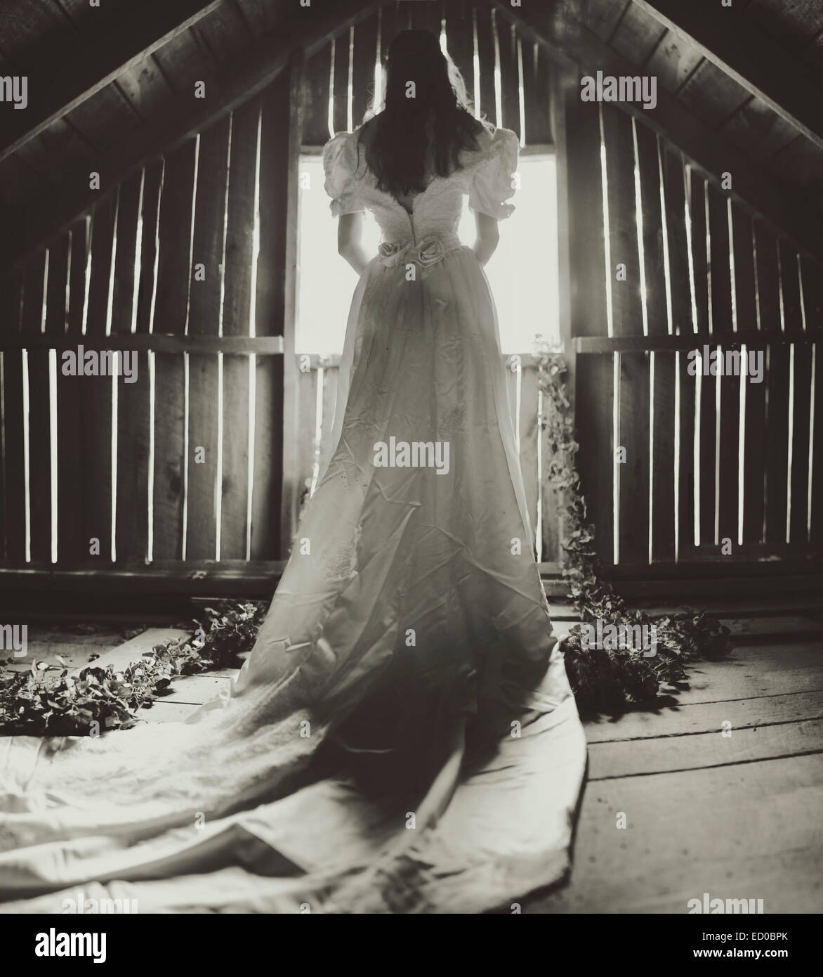 Rückansicht der jungen Frau in einem Hochzeitskleid, das aus einem Fenster schaut Stockfoto